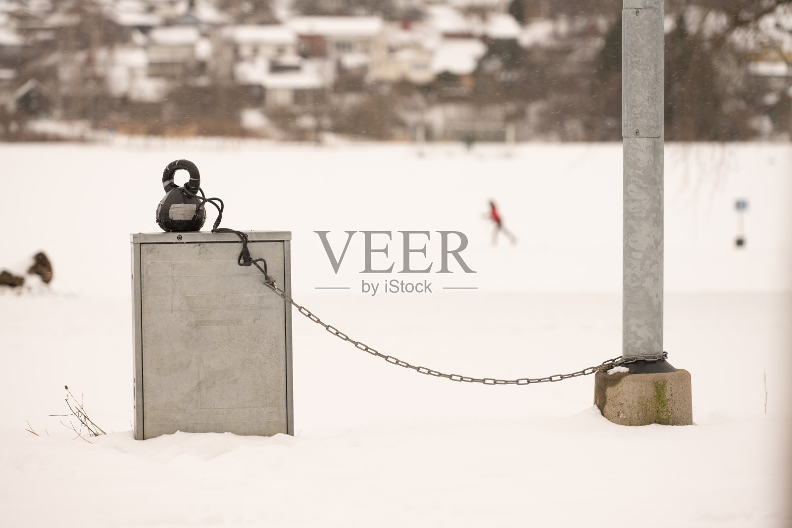 在一个下雪的公园里，用链子拴在灯杆上的壶铃。照片摄影图片
