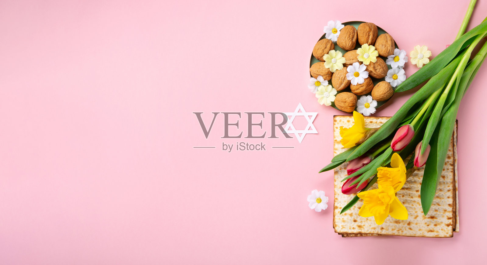 逾越节贺卡无酵饼，坚果和春天的花朵在粉红色的背景。照片摄影图片