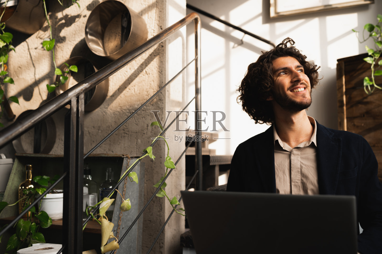 年轻的潮人坐在休息室的楼梯上使用笔记本电脑，看着窗外积极的脸。创意和小型企业概念照片摄影图片