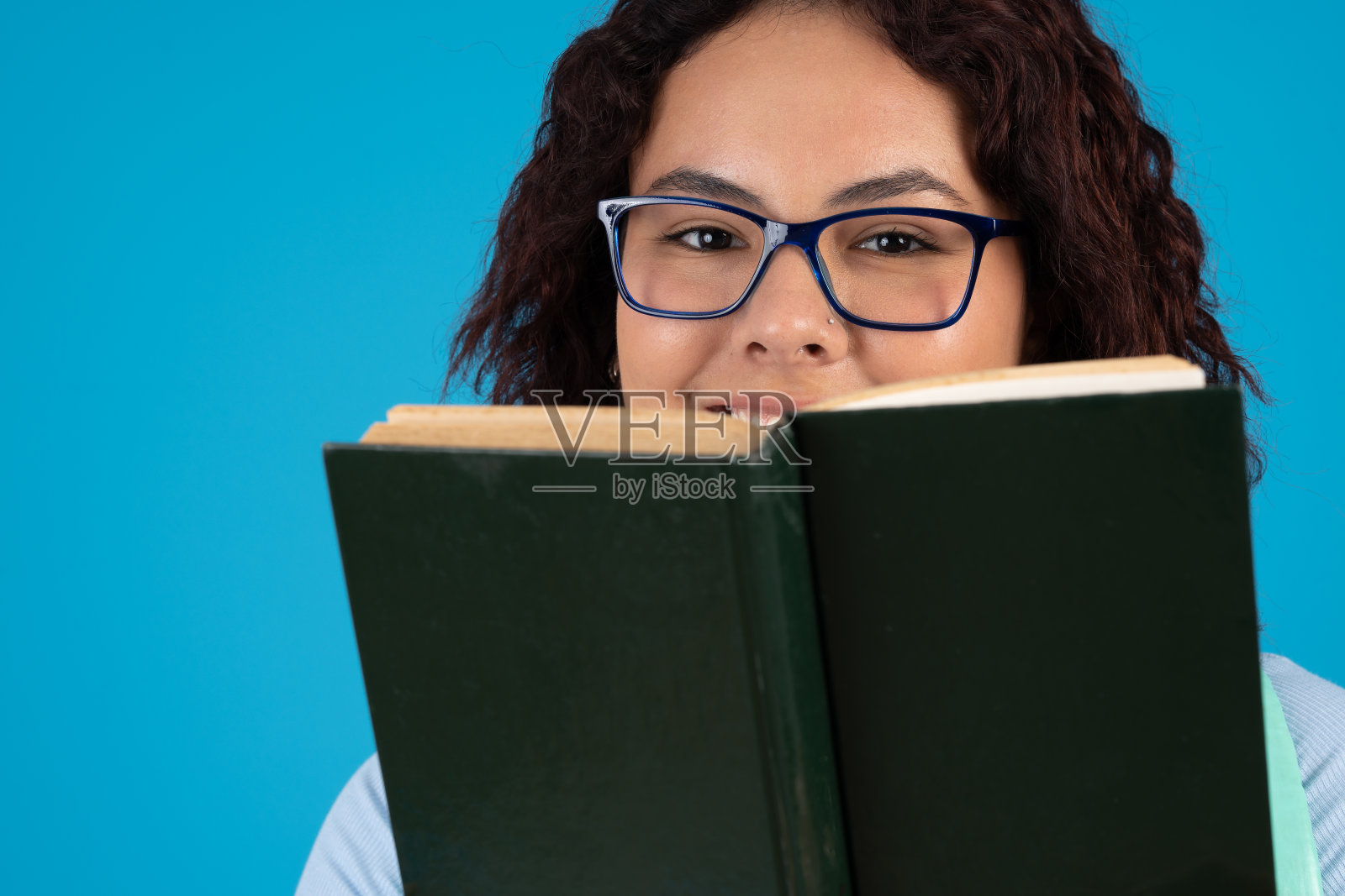 微笑的年轻女子戴着眼镜，看着相机，拿着一本精装书照片摄影图片