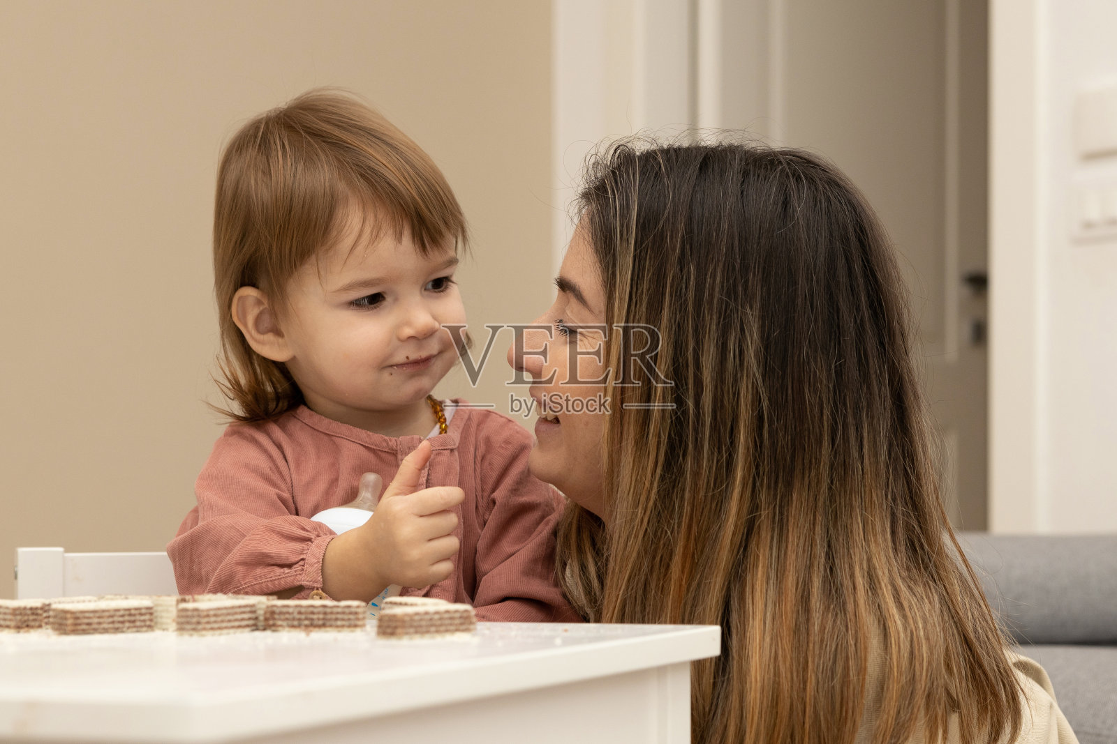 母亲和两岁的女儿在儿童餐桌旁互相微笑着吃华夫饼照片摄影图片
