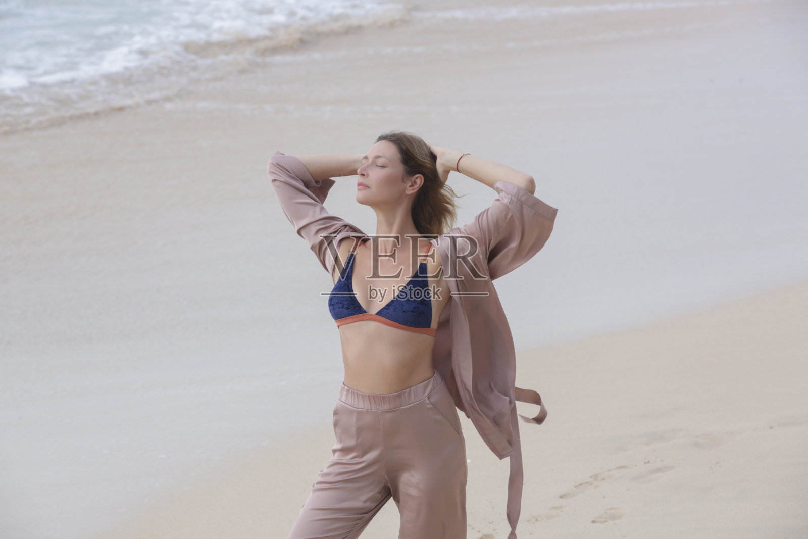 美丽安详的女人在沙滩上举起手臂，享受自然，自由和新鲜的空气，幸福的概念，正念和存在于当下。照片摄影图片