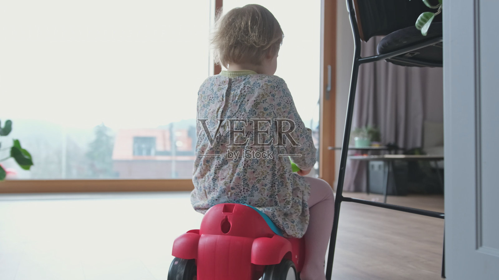 快乐的高加索女孩蹒跚学步的脚骑上玩具步行车在客厅和厨房有很多乐趣照片摄影图片