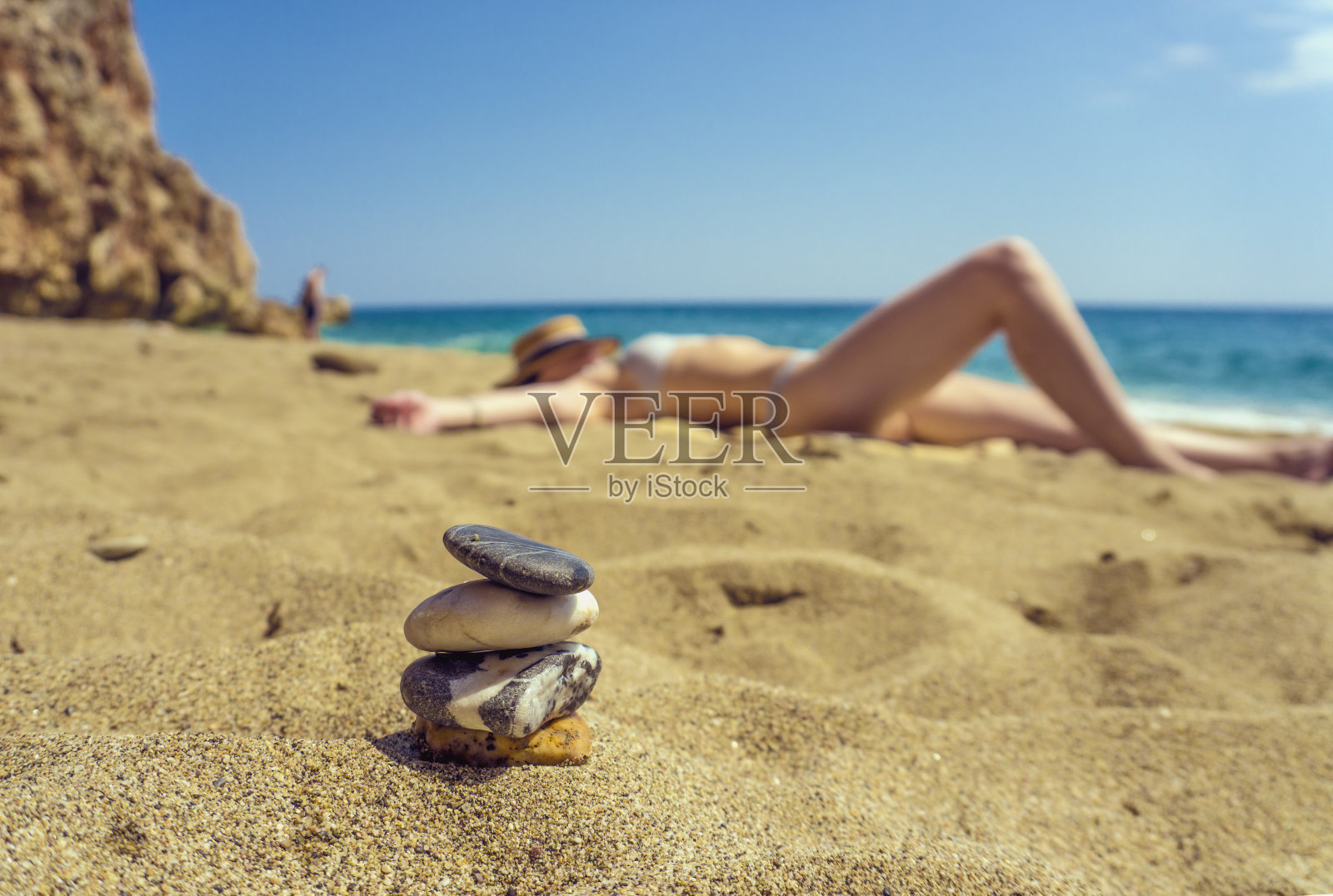 一个女人或女孩躺在海滩上，前景是一个石头平衡金字塔照片摄影图片