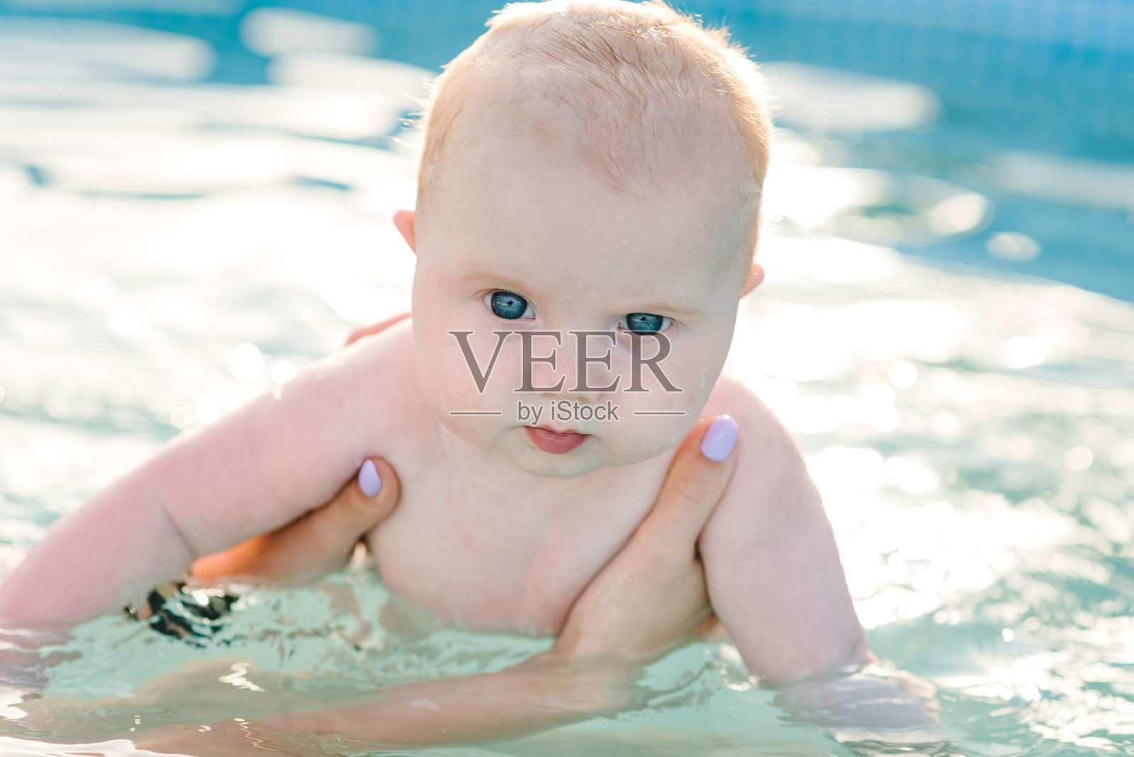 年轻的母亲，游泳教练和游泳池里快乐的小男孩。教幼儿游泳。享受在水里游泳的第一天。妈妈抱着准备潜水的孩子。做练习照片摄影图片