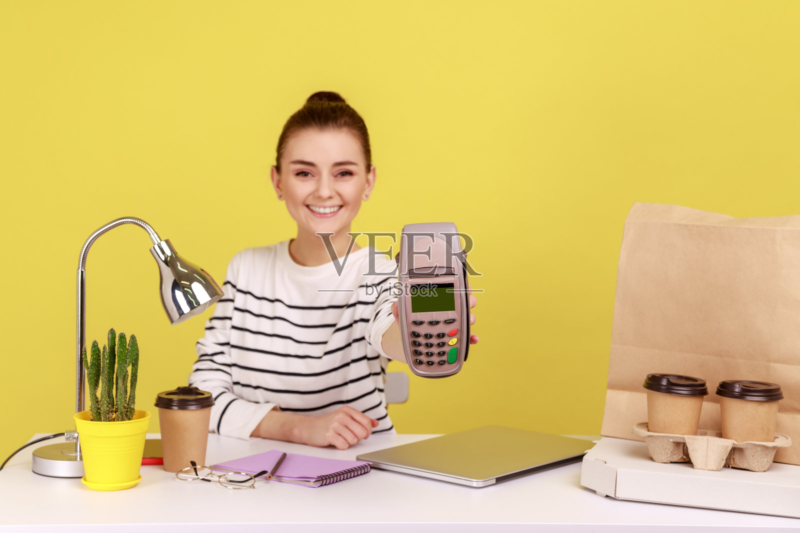 妇女坐在工作场所，手里拿着pos的非接触式支付终端。照片摄影图片