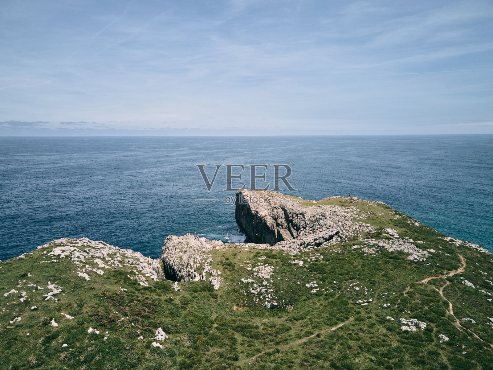 蔚蓝的天空下，西班牙ribadesella asturias海边，一条狭窄的小路穿过悬崖上的大石头上的草地照片摄影图片