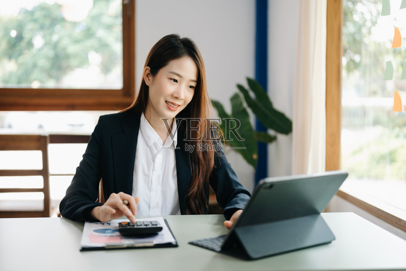 年轻漂亮的女人使用笔记本电脑和平板电脑，而坐在她的工作地点。专心工作。照片摄影图片