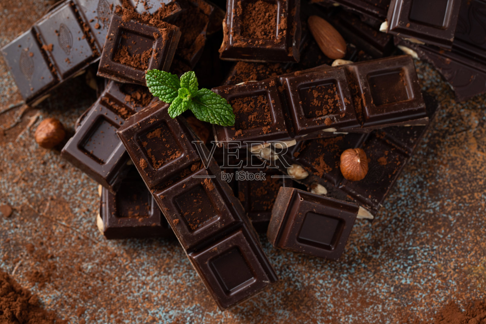 黑牛奶巧克力，黑色背景上撒有可可粉的坚果。照片摄影图片