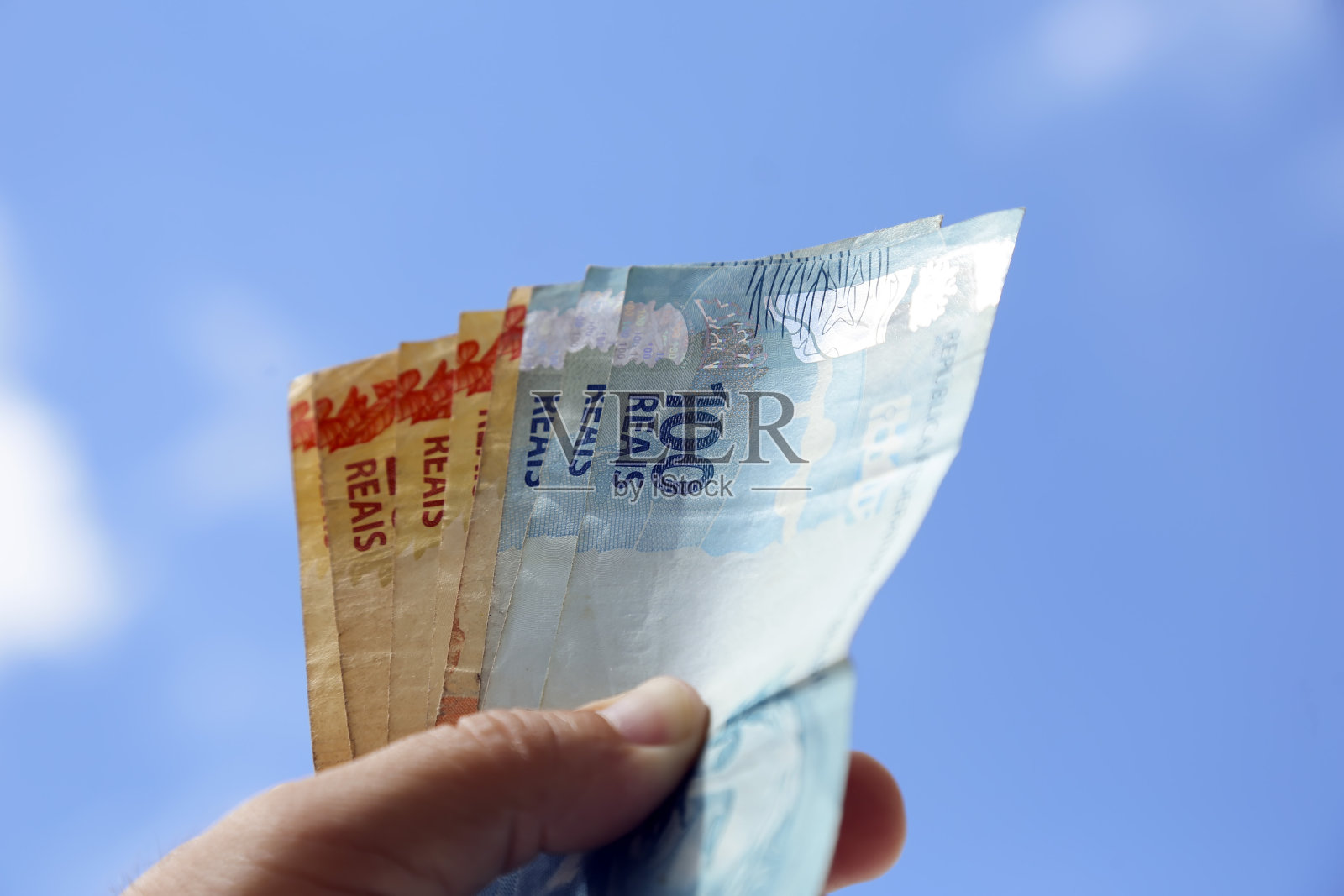 来自巴西的钱——拿着巴西真实钞票，背景是天空照片摄影图片