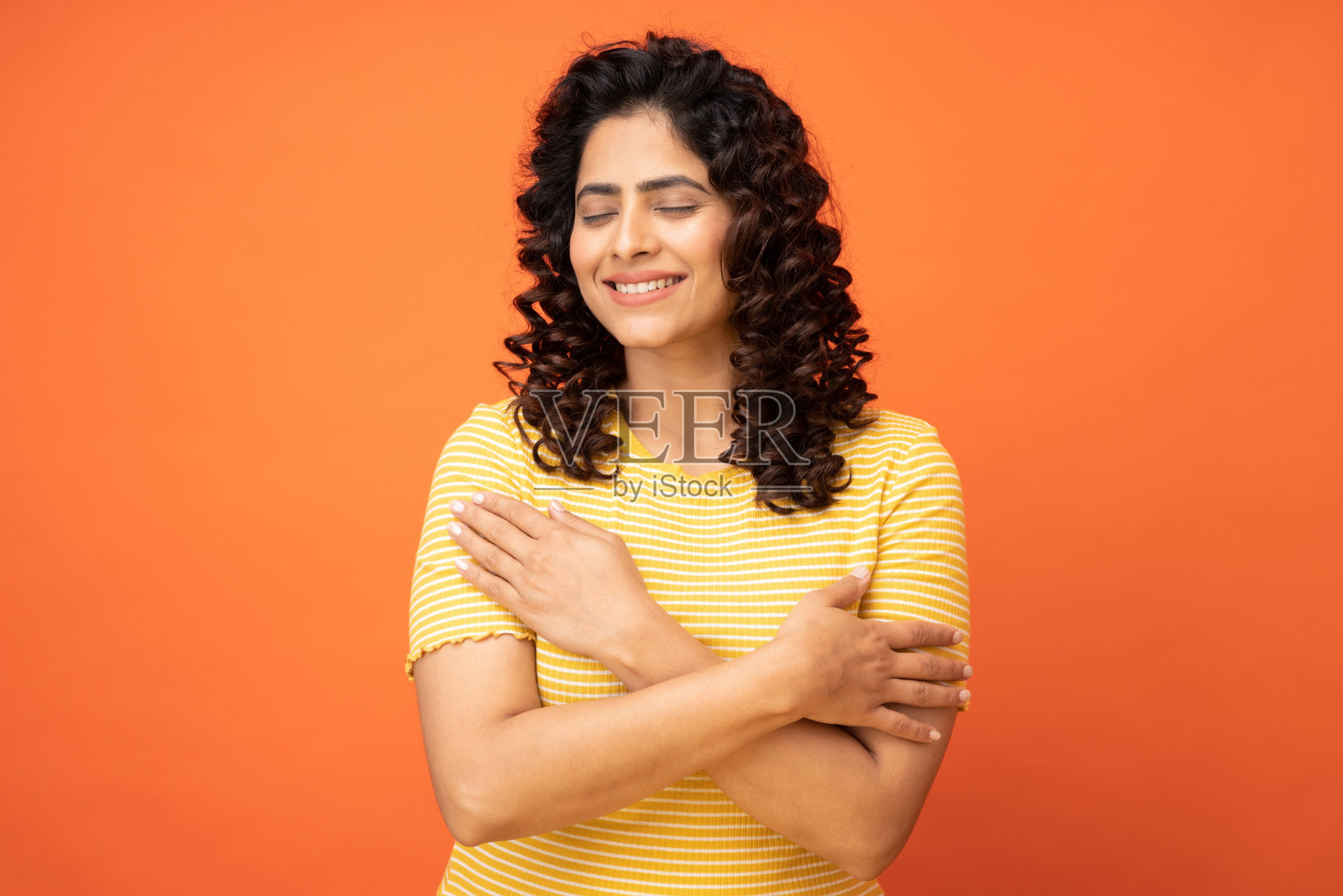 年轻女子交叉双手触摸漂亮的条纹套头衫孤立的橙色背景，股票照片照片摄影图片
