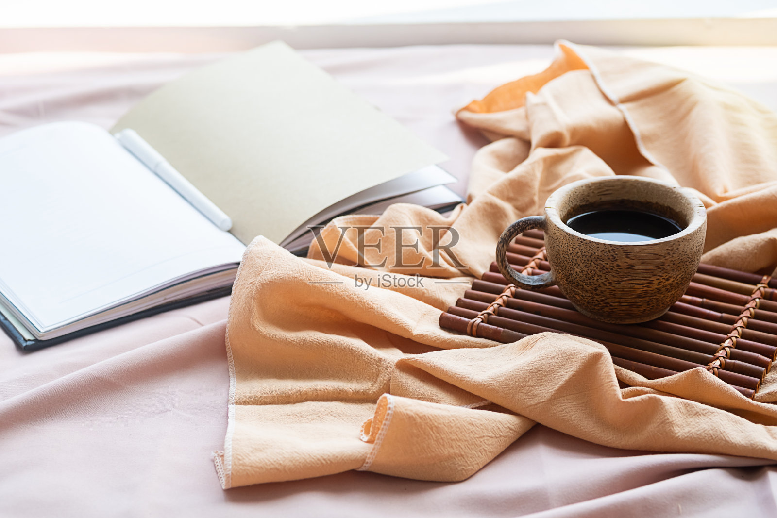 咖啡杯，竹托盘和打开的笔记本在床上。美好的春天早晨。照片摄影图片