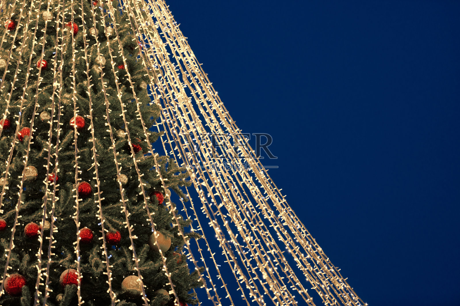 圣诞树上的彩灯以黄色的花环为夜晚蓝天的背景，复制空间照片摄影图片