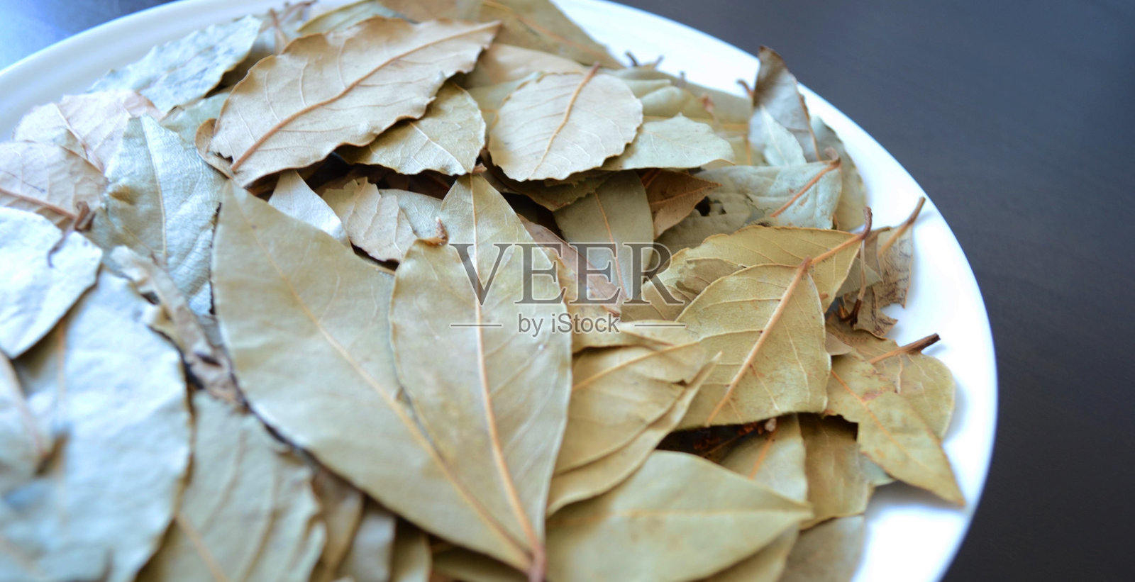照片的白色盘子与月桂叶在黑暗的木材背景，香料和调味料，干燥的植物照片摄影图片