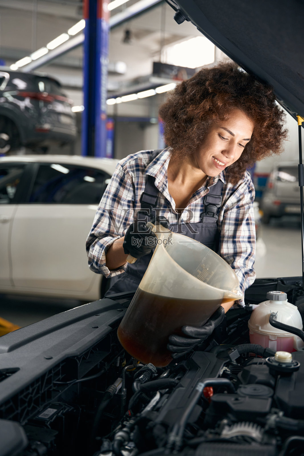 微笑的年轻汽车修理工将油注入发电机照片摄影图片