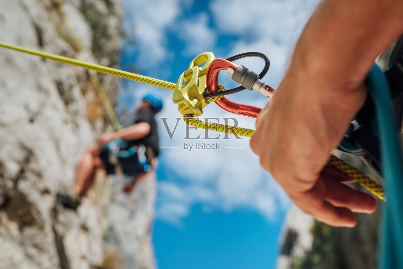 保护装置的特写镜头，一个男孩在悬崖上攀爬。他挂在一根攀岩绳索上，他的搭档在地上保护他。积极的人与运动的概念形象照片摄影图片