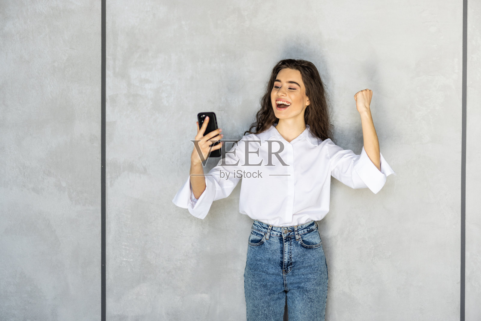 兴奋的年轻女子惊讶于难以置信的购物移动应用程序销售信息，看着智能手机孤立在白色背景上照片摄影图片