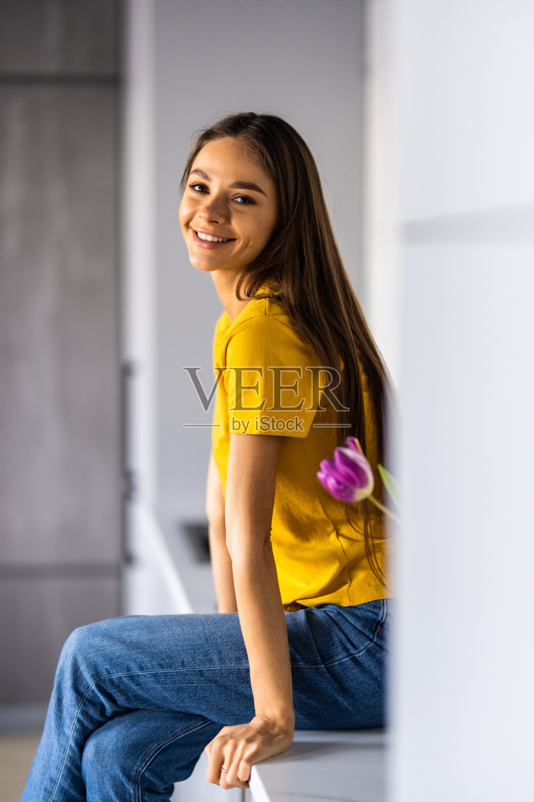 美丽的年轻微笑的女人在笔记本电脑上工作，喝咖啡，坐在厨房的台面在家里。照片摄影图片