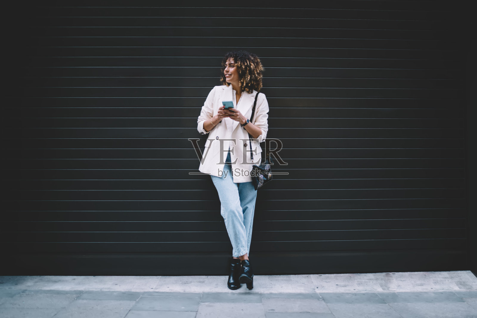 穿着时髦的女博主，手里拿着现代的手机设备，在促销的城市环境中休闲，快乐的潮女孩，带着智能手机，在时尚文本的复制空间附近微笑照片摄影图片