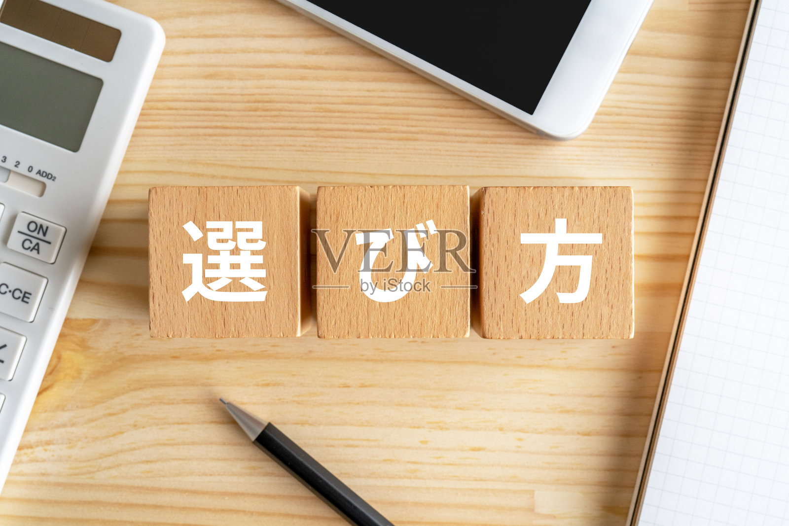 木块上有“erabikata”概念文本，一支笔和一个笔记本。照片摄影图片