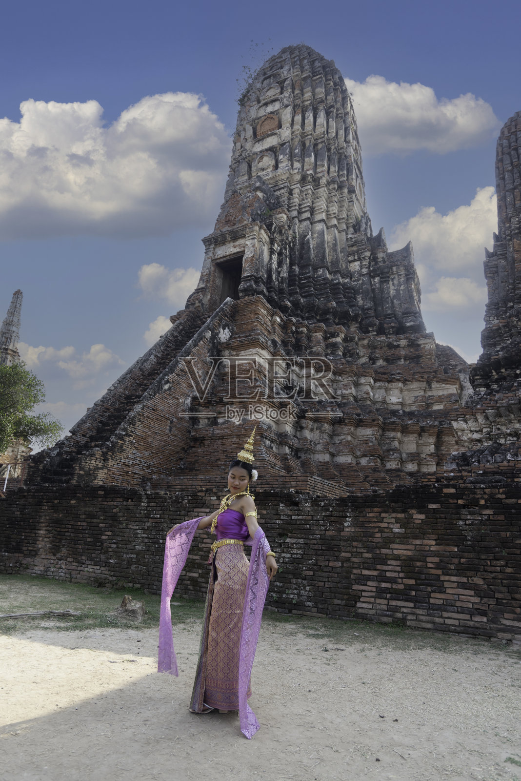 一名年轻女子穿着传统的泰国服饰，戴着金饰，站在古老的遗址Chaiwatthanaram寺，表示欢迎和问候。泰国民族服饰照片摄影图片