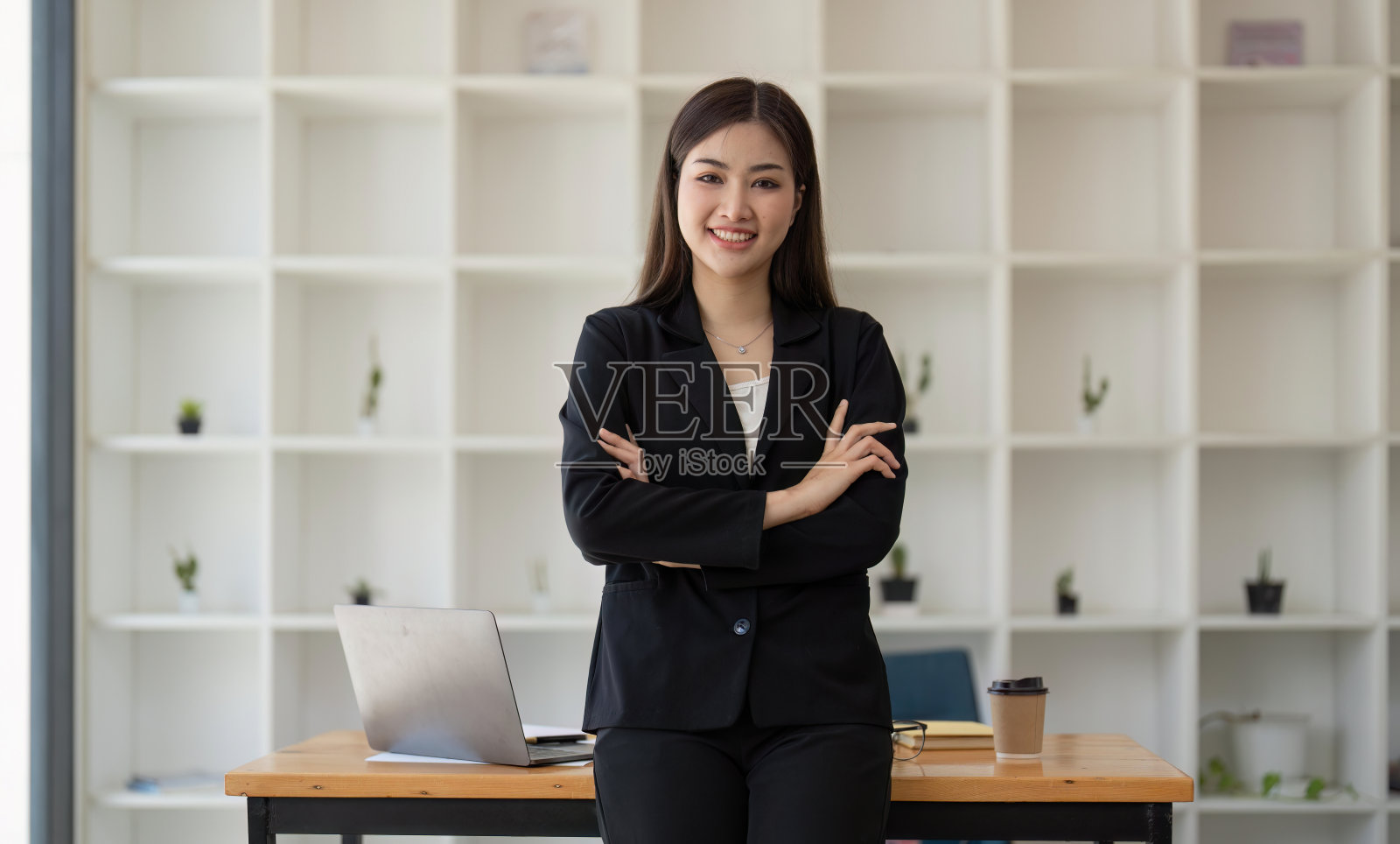 年轻成功的女企业家或上班族在现代化的办公室里，双手交叉站在桌子旁，微笑着看着镜头照片摄影图片