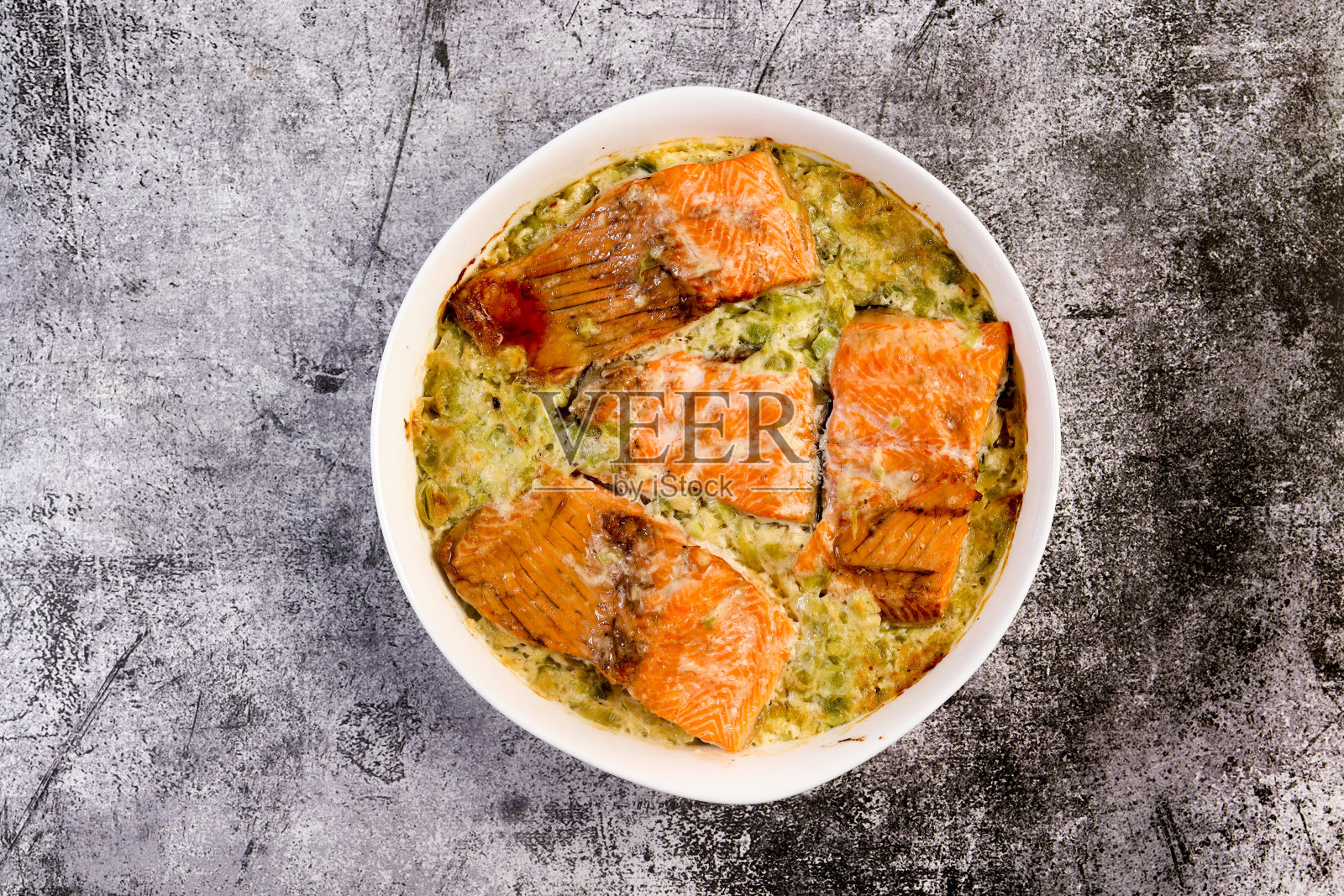 奶油烤三文鱼配韭菜，放在深灰色背景的白色烤盘中。俯视图，平面布局照片摄影图片