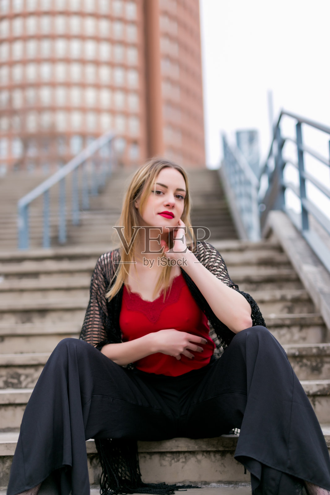 年轻漂亮的金发女人坐在城市的楼梯上照片摄影图片