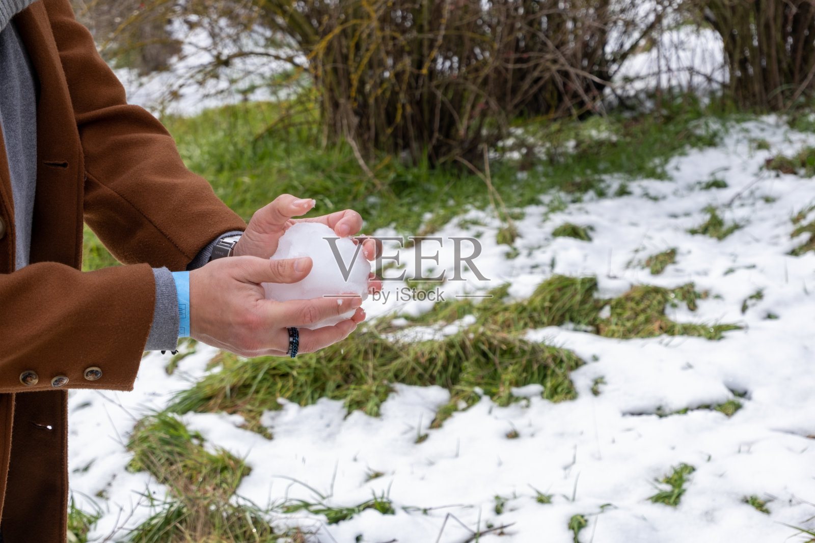 一个年轻的白人男子的手在布尔戈斯公园里做雪球，背景是白雪皑皑的草地。照片摄影图片