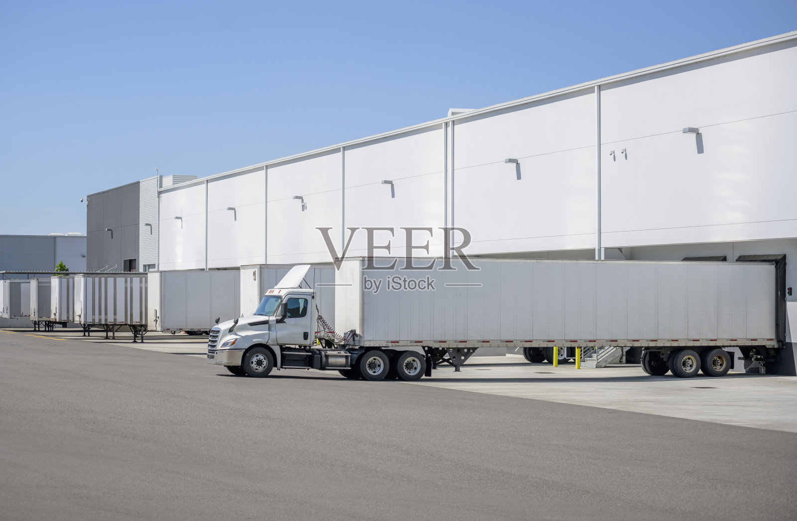 阳光明媚的工作日，带顶棚的白色大卡车和半挂车在仓库码头门口装货照片摄影图片