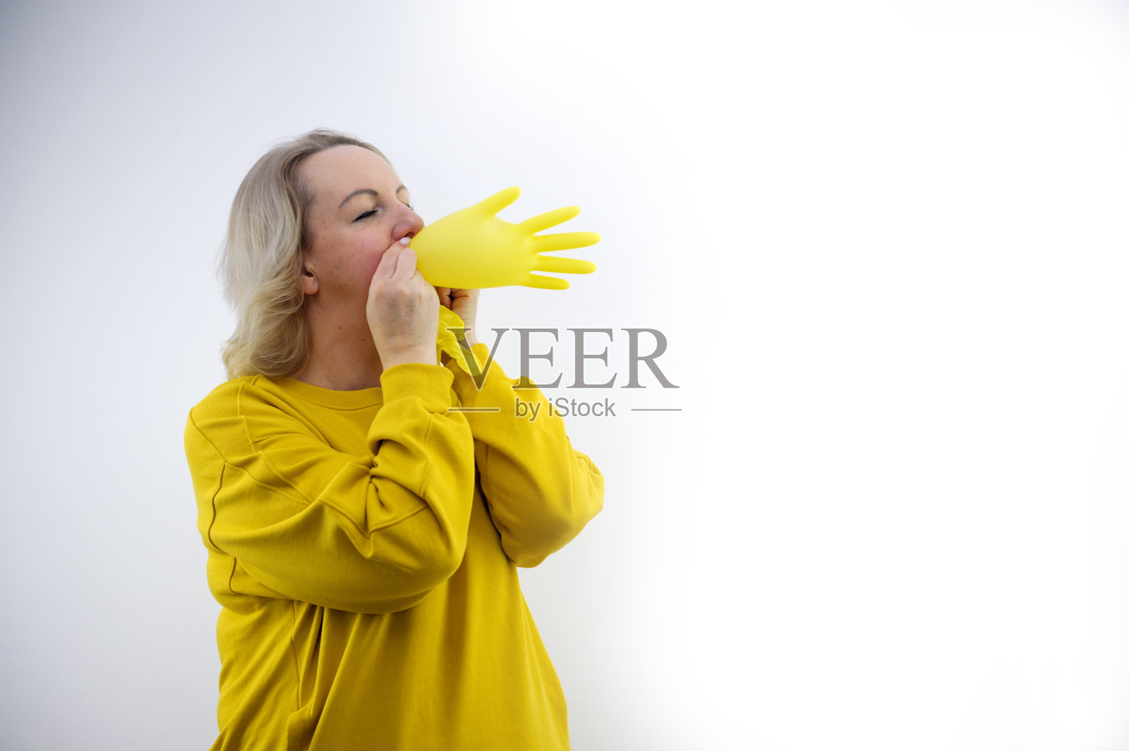 黄衣女子在白色背景上戴上明亮的黄色手套，为病人重现了欺骗的概念照片摄影图片