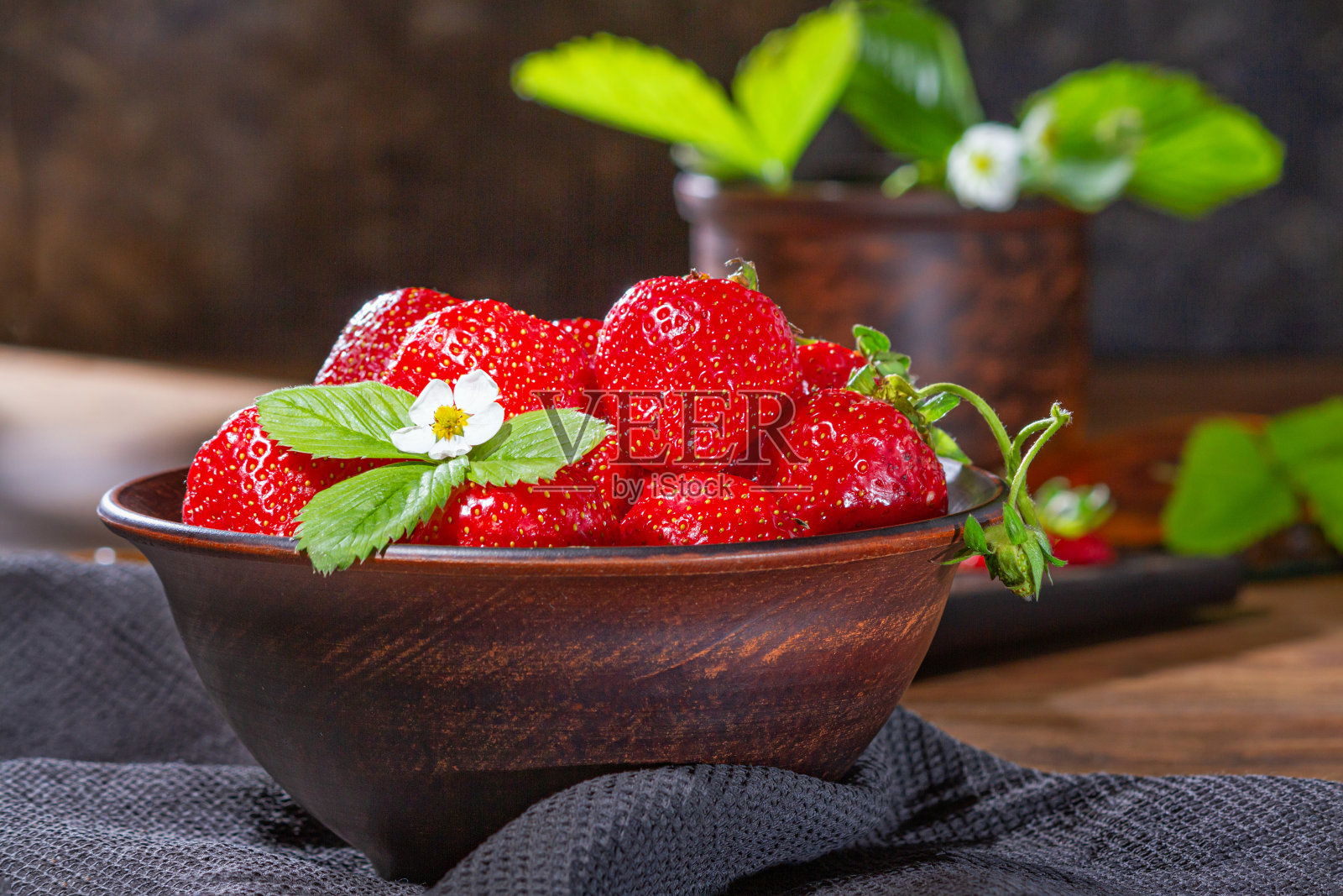 草莓装在木桌上的泥碗里。一碗多汁的新鲜成熟的红草莓照片摄影图片
