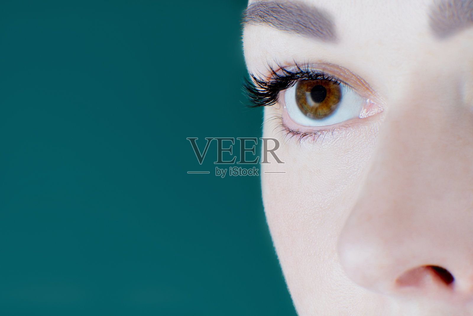 棕色眼睛的特写，人工睫毛，健康的皮肤，眉毛的不认识的年轻女子看向一边。照片摄影图片