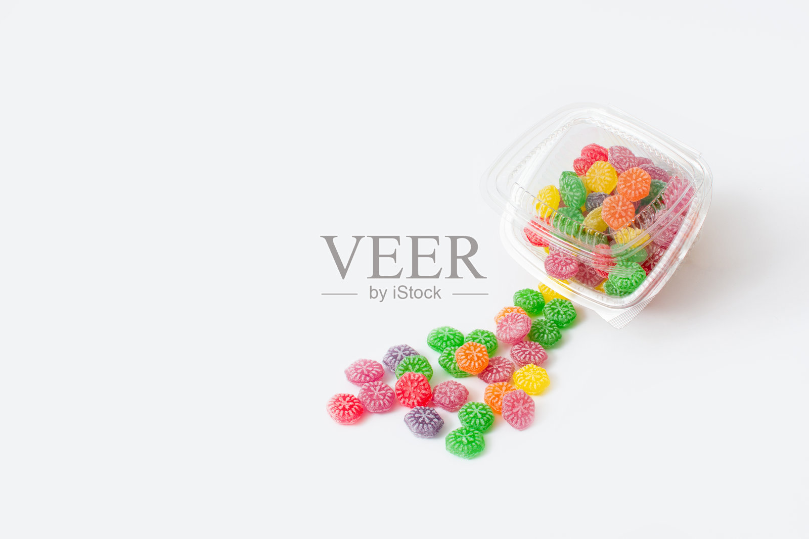 白色背景的塑料盒里装着美味的糖果。红色、绿色、黄色、橙色和紫色的糖果。甜食的现代概念。照片摄影图片