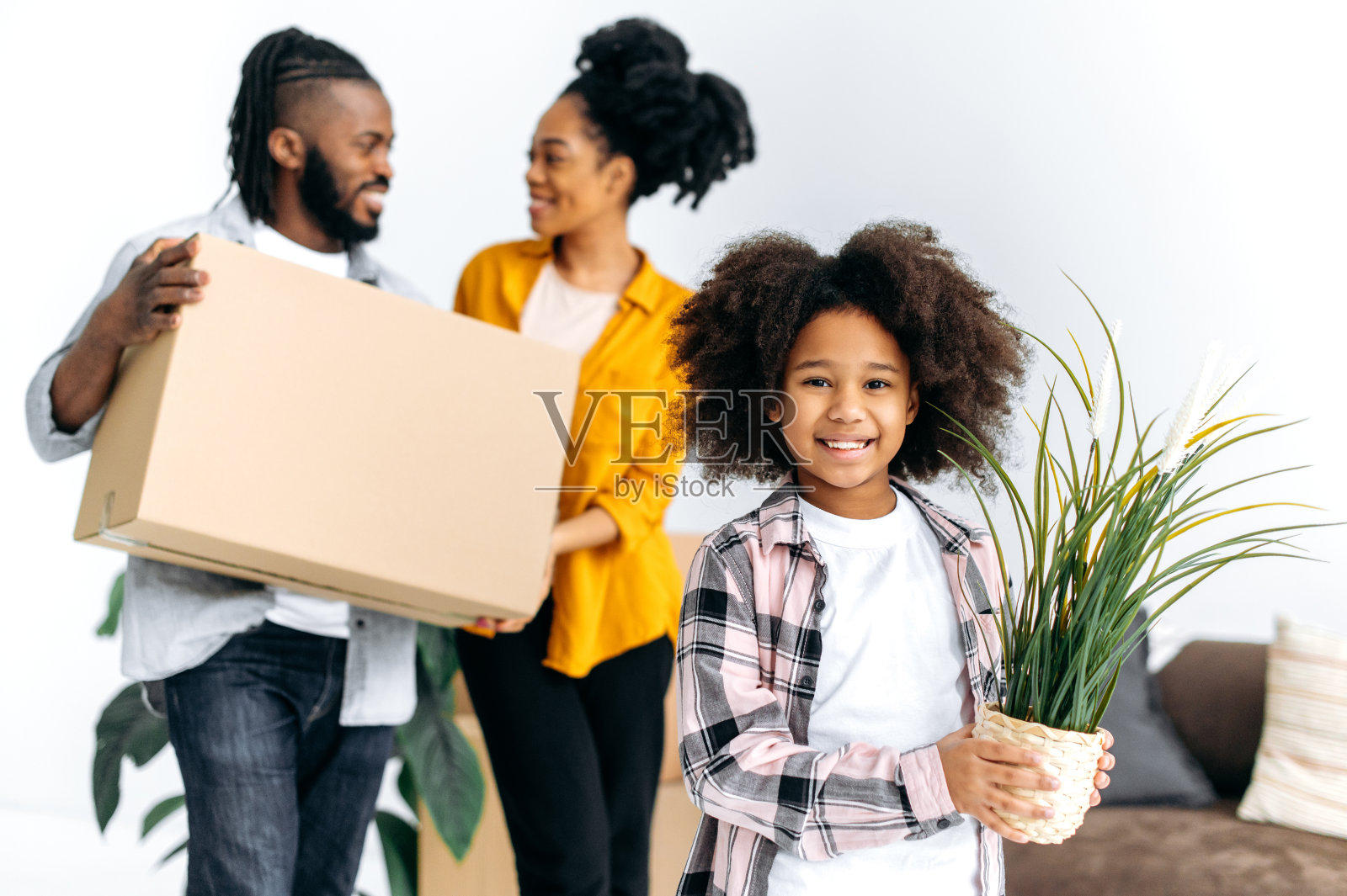 搬迁的概念。快乐的小非裔美国女孩捧着花盆，父母捧着纸箱，快乐的黑人家庭搬进新家，买了他们的第一套房子，投资了自己的房子照片摄影图片