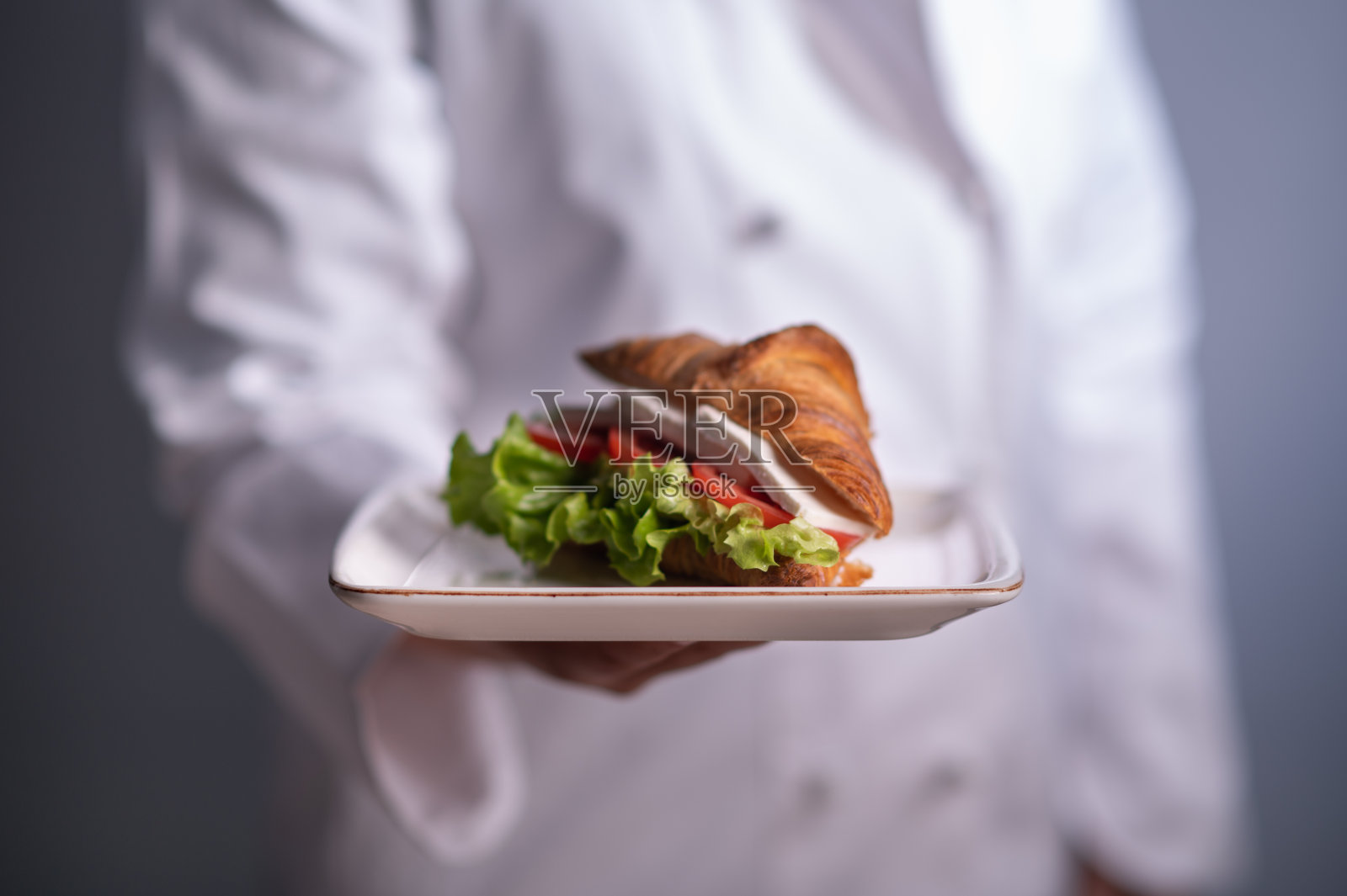 厨师端着盛有美味羊角面包三明治的盘子照片摄影图片