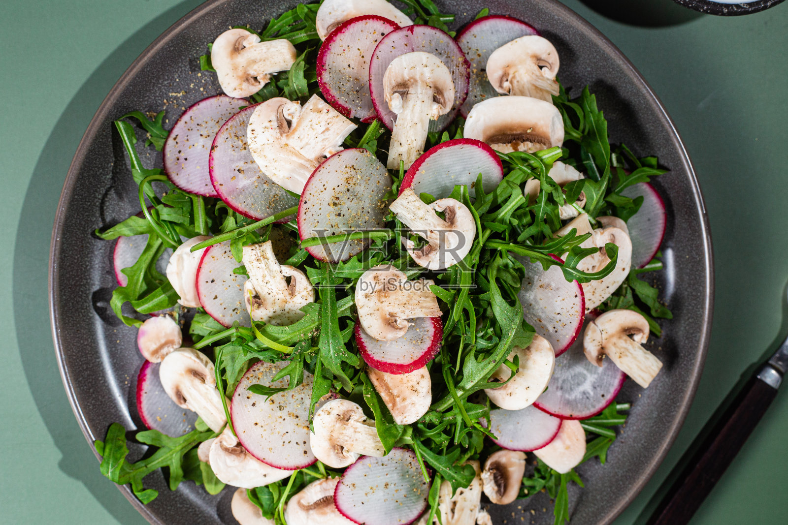 新鲜芝麻菜、萝卜和蘑菇的素食沙拉，盘子里有深色背景照片摄影图片