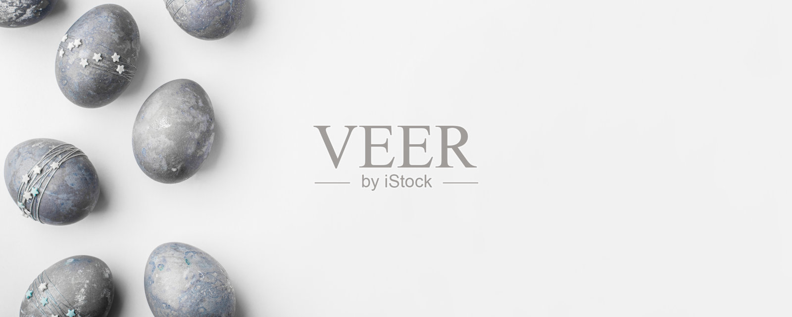 白色的桌子上放着星星的灰蓝色复活节彩蛋。照片摄影图片