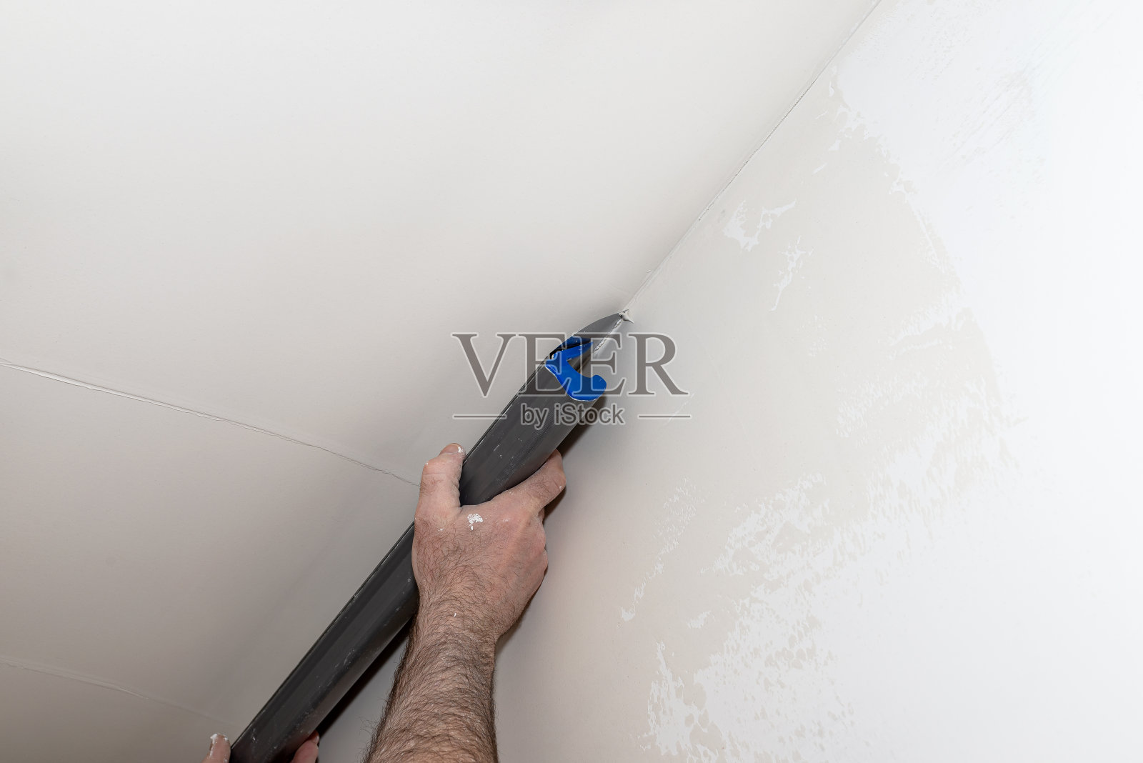 一名男子用特制的石膏切割器从桶中涂抹现成的聚合物石膏。照片摄影图片