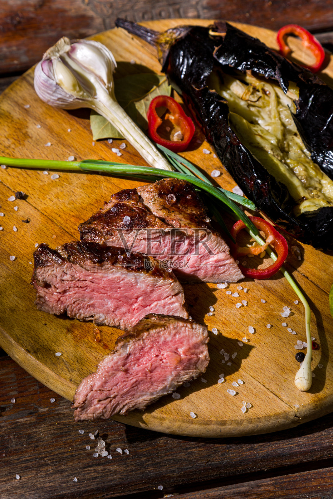 烧烤牛肉片，加上月桂叶、盐、红辣椒、大蒜、西葫芦和韭菜，放在圆形木板上。垂直方向照片摄影图片