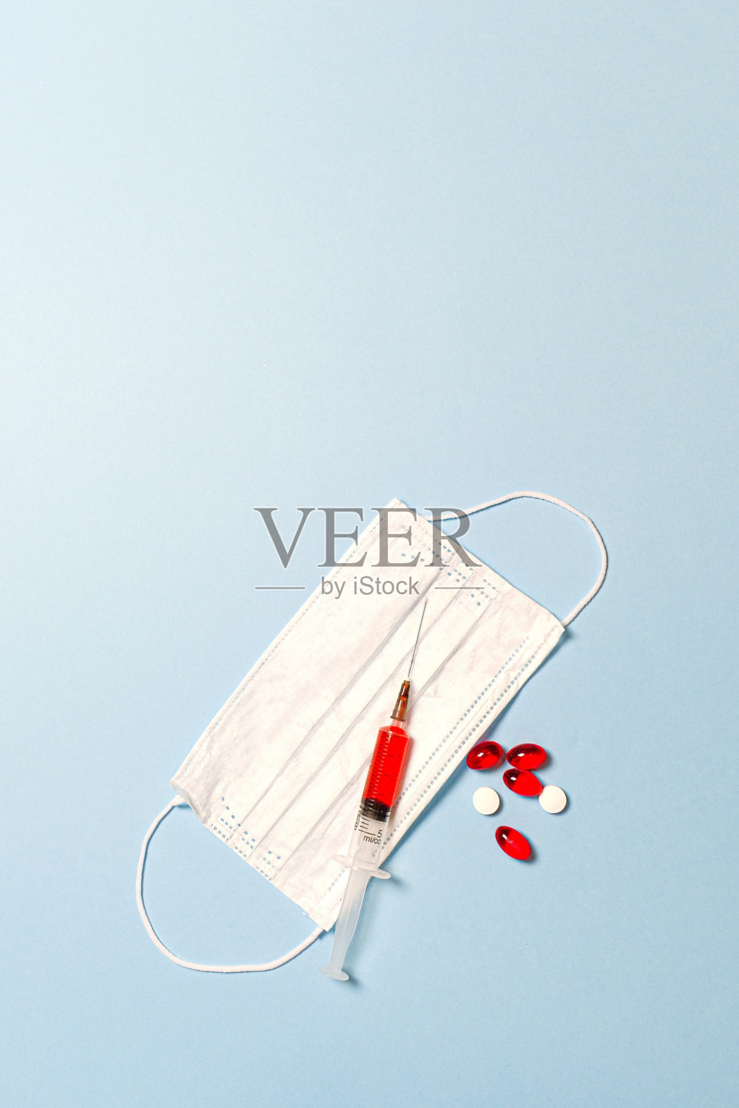 浅蓝色背景上已经含有疫苗、口罩和维生素药物的注射器照片摄影图片