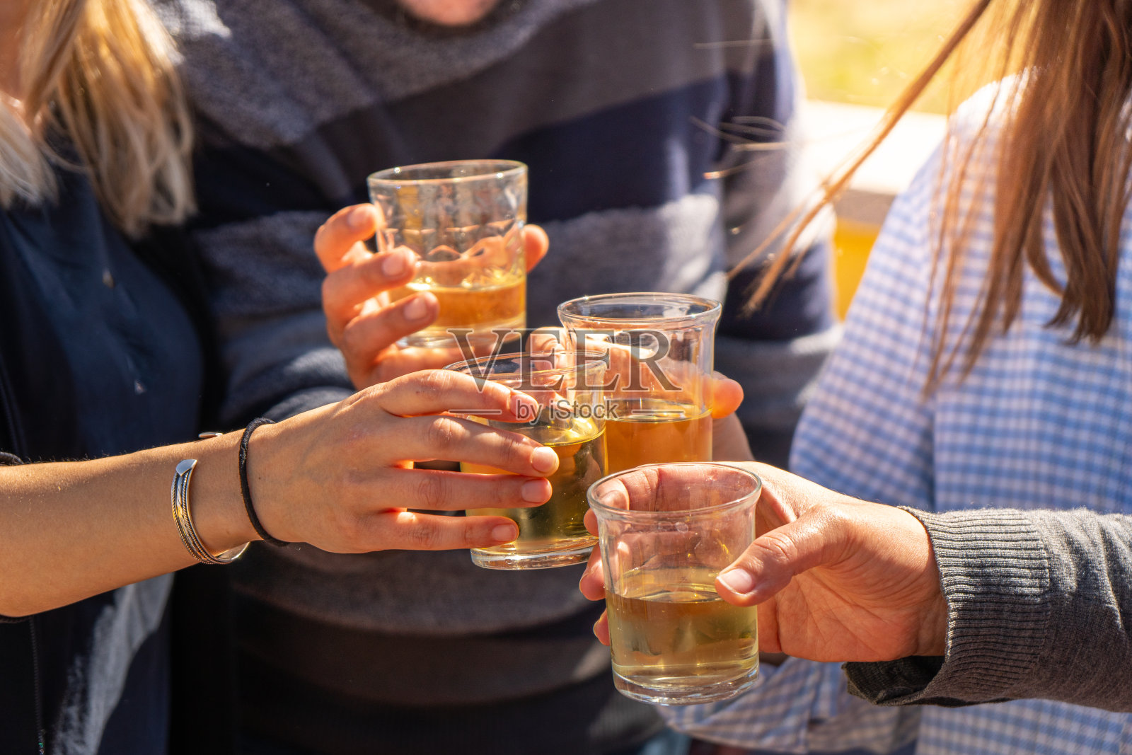 四个朋友的手碰着白葡萄酒，在一个阳光明媚的日子里点燃他们的杯子，举杯再次相聚的细节。照片摄影图片