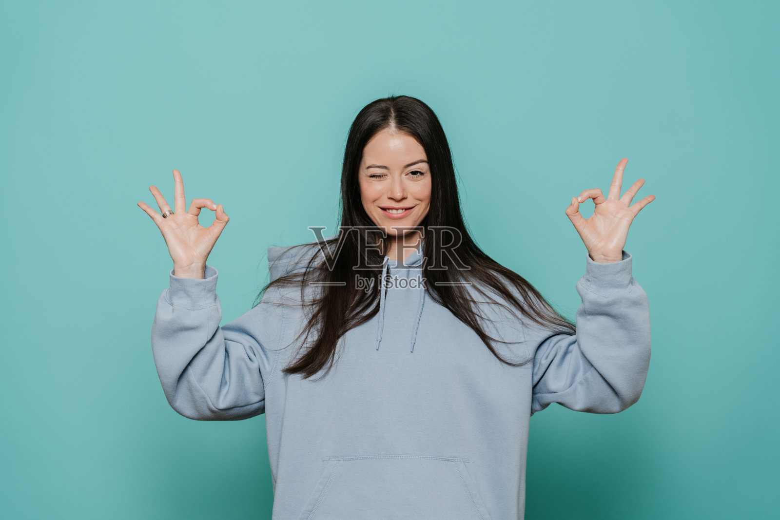 我做到了。满意的年轻漂亮的女人在超大帽衫，在顽皮的情绪眨眼，显示ok的手势，高兴因为她失去了很多体重后，她的饮食和健身。保健健身理念。照片摄影图片