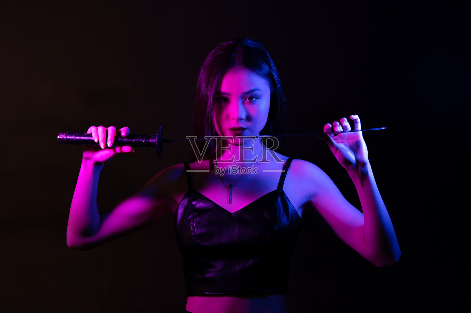 在霓虹灯下，年轻美丽的亚洲女子手持武士刀。照片摄影图片