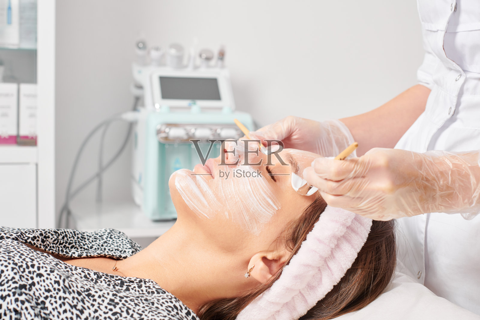 美容师在美容院为女性面部涂抹美容霜面膜以恢复青春照片摄影图片