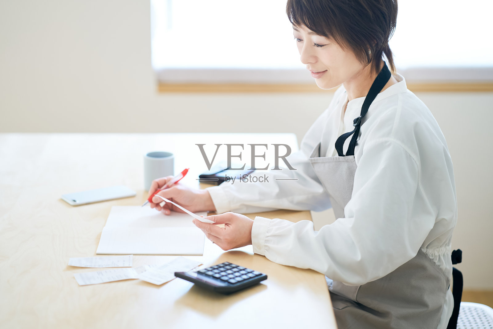 一个围着围裙的女人在检查收据照片摄影图片