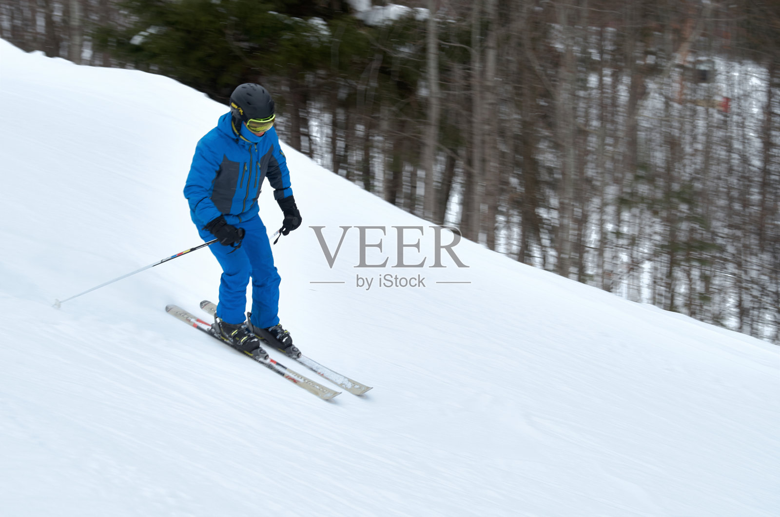 一个穿着蓝色运动服的男人踩着滑雪板从雪坡上滑下来照片摄影图片