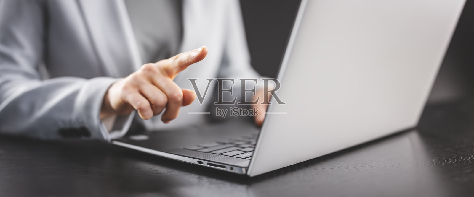 女商人坐在黑色的桌子上，用手指指着她笔记本电脑的显示屏。照片摄影图片