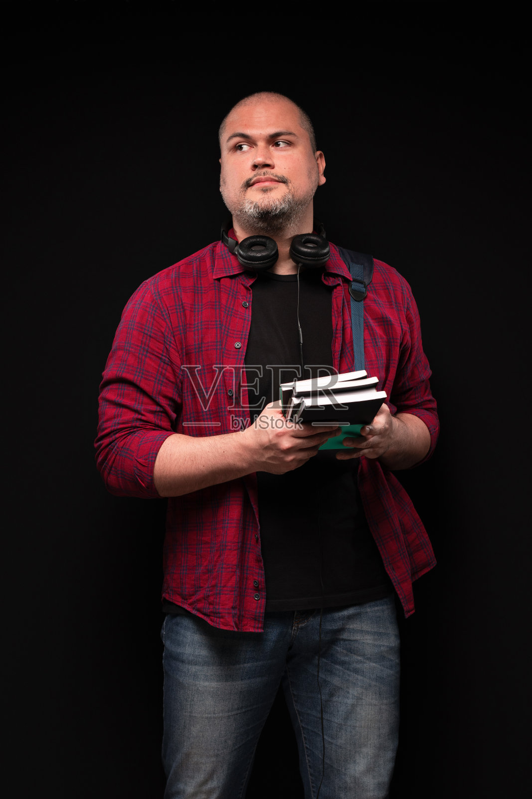 一个巴西男人的肖像，背着背包，戴着耳机，手里拿着书，看着一边，穿着红色衬衫和蓝色牛仔裤-彩色照片-巴西照片摄影图片