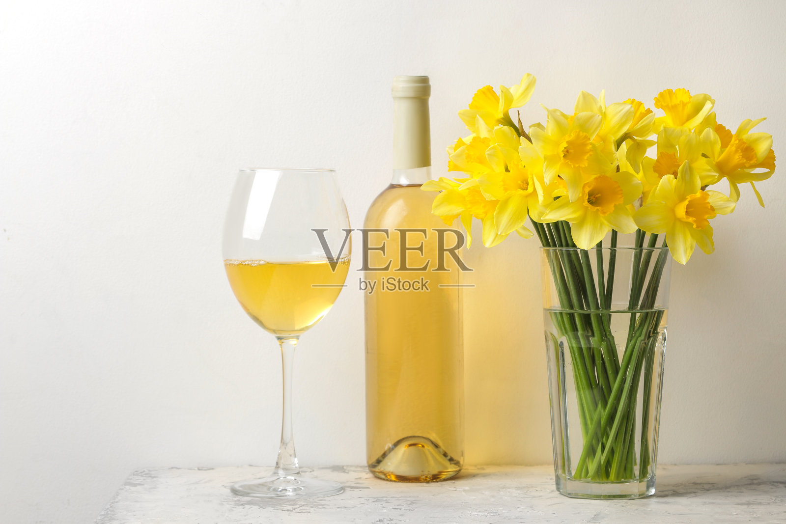 一束春天的花，花瓶里的水仙花，浅色背景上的一杯酒照片摄影图片
